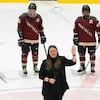 Postée devant quatre joueuses de hockey, une femme se tenant debout au centre d'une patinoire salue la foule en souriant.