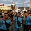 Des partisans avec des chandails aux couleurs de Manchester City posent pour la caméra devant un trophée et un ballon de soccer géants.