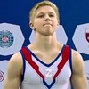 Un jeune gymnaste porte un uniforme bleu, blanc et rouge sur lequel on peut voir un z en ruban adhésif