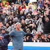 Un joueur de tennis sourit et tend les bras, avec sa raquette dans la main droite. La foule l'applaudit.   