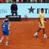 Un joueur de tennis en regarde un autre, qui marche avec une serviette sur l'épaule.