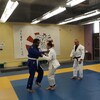 Un judoka en bleu tient par son judogi son adversaire en blanc sous les regards d'un entraîneur