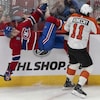 Un joueur de hockey est entrain de tomber sur la glace alors qu'un adversaire vient de le plaquer contre la bande.