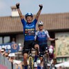 Un cycliste en bleu lève les bras en triomphe.