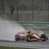 Lando Norris au volant de sa McLaren orange et noire sur le circuit de Shangai, sous la pluie. Une grande gerbe d'eau s'élève derrière la voiture. 