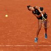 Une joueuse de tennis vêtue de noir regarde la balle qu'elle vient de servir. 