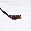 Un bâton de hockey se trouve sur la patinoire avec du ruban aux couleurs de l'arc-en-ciel.