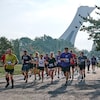 De nombreux coureurs foulent la piste du Parc olympique de Montréal, avec le stade en arrière-plan.