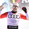 Un skieur tient un petit globe de cristal dans sa main droite et lève les bras.