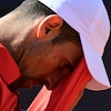 Un joueur de tennis essuie son front avec son chandail.