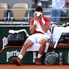 Un joueur de tennis est assis sur son banc et passe une serviette sur son visage pendant une pause.