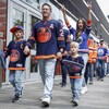 Deux enfants et deux adultes, portant des chandails des Oilers, marchent en direction d'un amphithéâtre.