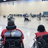 Des spectateurs regardent un match de soccer disputé par des joueurs en fauteuil roulant motorisé.