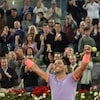 Un joueur de tennis lève les deux bras et sourit devant une foule qui l'applaudit.