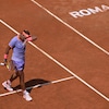 Un joueur de tennis marche et s'éponge le front de la main gauche sur un terrain en terre battue. 