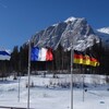 Des drapeaux de plusieurs pays flottent devant une chaîne de montagne.