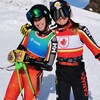 Deux skieuses souriantes, en combinaison de vitesse posent pour la photo sur une pente enneigée.