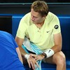 Un joueur de tennis, assis et résigné, est soigné au poignet droit sur le terrain.