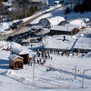 Vue en plongée d'un chalet entouré de plusieurs skieurs, en hiver.
