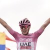 Un cycliste, vêtu de rose, lève les bras en signe de victoire.