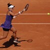 Une joueuse de tennis vêtue d'une robe mauve et d'une casquette blanche frappe la belle du coup droit lors d'un match sur terre battue. 