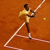 Un joueur de tennis court et étire le bras pour frapper la balle pendant un match disputé sur terre battue.