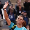 Un joueur de tennis, sac à l'épaule, envoie la main aux spectateurs qui l'entourent.