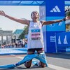 Une femme s'agenouille et tend les bras vers le ciel à l'arrivée d'une course.