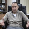 Assis sur un fauteuil dans un bureau, l'homme répond à une question.