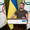 Il se tient debout devant des drapeaux ukrainiens et olympiques lors d'une conférence de presse. 