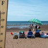 Vue rapprochée d'un thermomètre indiquant 31 degrés Celsius et en arrière-plan des gens sur une plage.