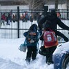 Des enfants marchent dans la neige avec leur parent vers la cours d'école. 