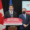 Justin Trudeau devant un lutrin. Derrière lui se tient M. Legault portant un masque.