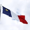 Un grand drapeau de l'Acadie flotte au sommet d'un mât.