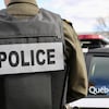 Un patrouilleur de la Sûreté du Québec avec gilet pare-balle de dos près de son véhicule auto-patrouille.