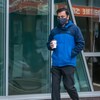 Un homme marche dans la rue, tenant un café dans la main, portant un masque. 