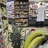Des étalages d'épicerie remplis. On voit des bananes dans un panier à l'avant-plan et un employé qui s'affaire à l'arrière-plan.