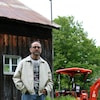 Stéphane Gendron pose devant un bâtiment agricole et un tracteur.