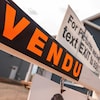 Affiche noire écrit « Vendu » en lettres orange devant une maison.