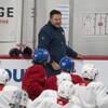 Un entraîneur de hockey parle à ses joueurs devant un tableau, en bordure de la patinoire.
