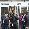 Un agent de sécurité est debout au milieu de nombreuses personnes agglutinées devant l'entrée du Complexe Guy-Favreau, à Montréal.