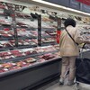 Une personne dans une allée d'épicerie devant le comptoir des viandes.