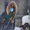 Une femme masquée marche dans la rue sous la neige.