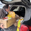 Un homme place un panier de provisions dans le coffre d'une voiture.
