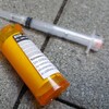 Une seringue usagée et un flacon débouché sur lequel est apposée une ordonnance de naloxone gisent sur le pavé.