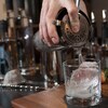 Un barman verse du gin d'un mélangeur dans un verre avec un glaçon.