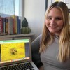 Une étudiante universitaire aux longs cheveux blonds, souriante, est assise à côté de son écran sur lequel apparaît une de ses photos de moules zébrées.