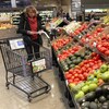 Une femme consulte sa liste d'épicerie dans un rayon de fruits et légumes.
