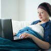 Une jeune femme atteinte du cancer regarde une vidéo sur un ordinateur dans son lit.