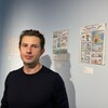 Portrait de Gallet d'Econova Educaiton devant des planches de bande dessinée accrochées à un mur de galerie.